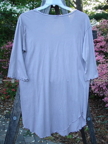 Barclay Batiste Round Bottom Shirt Unpainted Lavender Size 1, displayed on a hanger, features a deep neckline, curly edgings, three-quarter sleeves, and a rounded, vented hemline with drop shoulders.