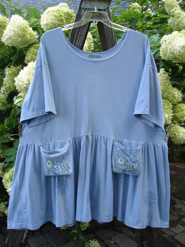 Barclay Collector's Tunic Dress Starburst Faded Sky Size 2: A blue shirt with exterior painted pockets on a wooden pole.