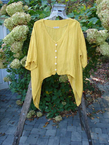 Barclay Rib Silk Dip Side Button Jacket in Golden Sunshine, featuring a V-neck, asymmetrical hem, and elbow-length sleeves. Displayed outdoors, highlighting its lightweight, flowing silhouette and pearly buttons.