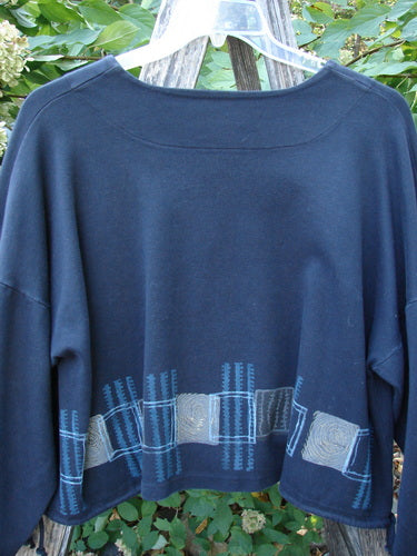 1999 Interlock Side Tie Jacket Fall Grid Black Size 2 displayed on a hanger, showcasing its wide A-line shape, decorative hem band, and unique drawcord sides against a leafy outdoor backdrop.