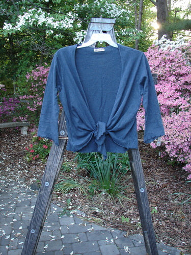 Barclay Hemp Cotton Long Pinch Sleeved Shrug Unpainted Navy Size 1 displayed on a wooden ladder, showcasing front tie wrap, deep V neckline, and pinched sleeves, highlighting its versatile and stylish design.