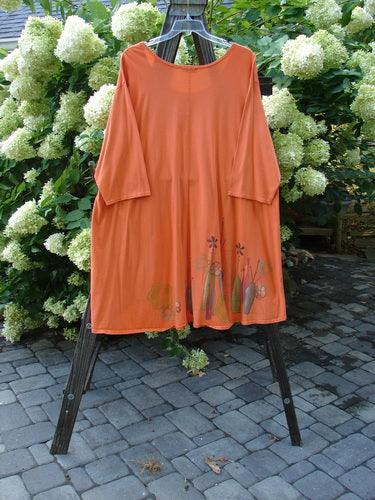 Alt text: Barclay Hi Low Tunic Top in Tangerine, made from Organic Cotton, displayed on a rack. Features include a soft neckline, varying hemline, and longer three-quarter sleeves. Size 2.