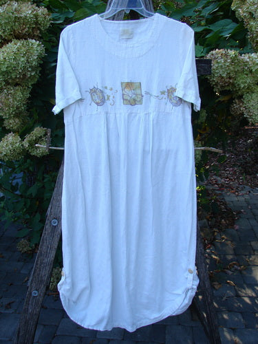 1999 Textured Linen Water Dress Garden Friends White Size 0: Loose-fitting white dress with a round neckline, embroidered floral panels, gathered waist, pleated skirt, and side tab-button hem, hanging outdoors.
