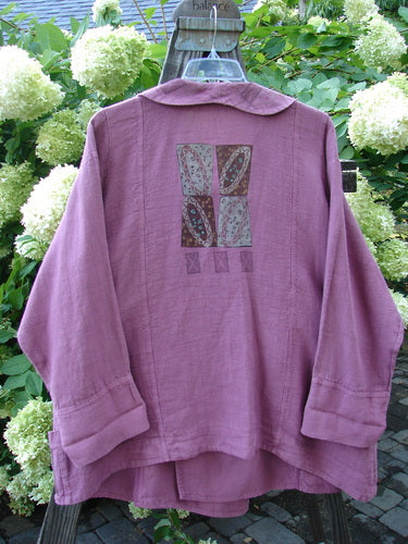A purple hemp jacket with a folded layered neckline, wooden toggle, and varying hemline. Features sectional panels, a rear rounded collar, and exterior stitchery. Size 2.