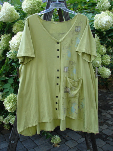 A Barclay Deep V Neck Button Pocket Cardigan in Sprout, featuring a mosaic floral theme paint. Made from medium-weight organic cotton, this cardigan has a deeply shaped neckline, wider short sleeves, and an A-line flair. The front hemline is scooped upward, and there is an exterior drop side painted pocket. The cardigan also has three sets of three button groupings. Bust: 56, Waist: 56, Hips: 60, Sweep: 75, Front Length: 33, Back Length: 37 inches.