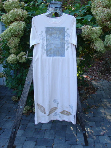 1999 Straight Dress Window Chair Teadye Size 0 hangs on a wooden ladder, featuring a grid motif on the chest, floral side outlines, leaf graphics near the hem, and rounded neckline.