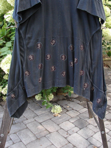 A black tunic dress with wrap-around side seams, oversized front pockets, and a scooped hemline. Made from organic cotton, it features a faded rose design. Size 2.