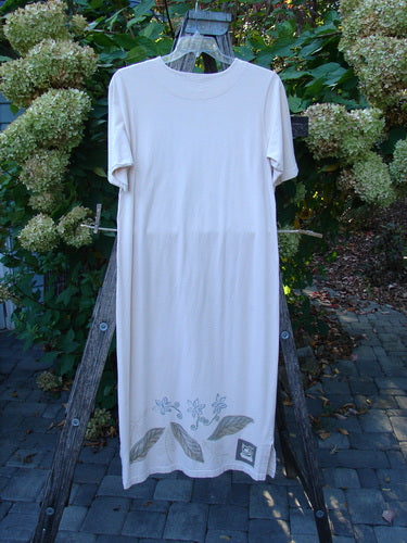 1999 Straight Dress Window Chair Teadye Size 0, off-white short-sleeve with floral motif on hem, displayed on a wooden A-frame outdoors. Organic cotton, rounded neckline, side pockets, vented hem.