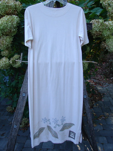 1999 Straight Dress Window Chair Teadye Size 0 displayed outdoors, features a knee-length organic cotton design with side entry pockets, subtle floral hem motif, and a round neckline, hanging on a wooden frame.