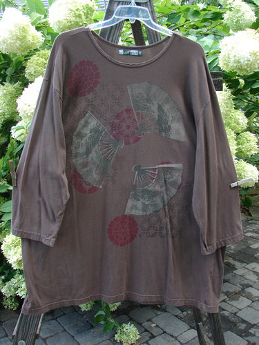 Image: A brown shirt with a fan design on it, close-up of a person's leg, and a close-up of a flower.

Alt text: Barclay Long Sleeved Café Tunic Top with Fan Fare design, featuring a brown shirt and intricate details.