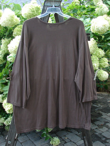 Image: A long-sleeved Barclay Café Tunic in mocha color, featuring a giant fanfare theme paint. The tunic is worn by a person swinging on a wooden post.