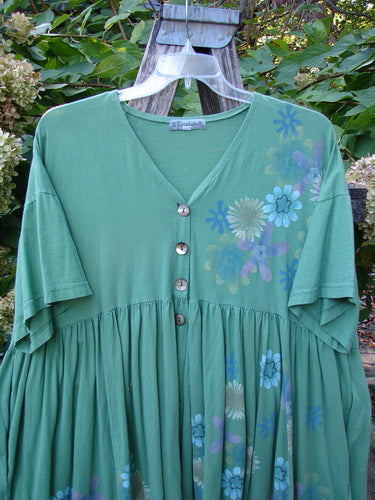 Barclay Tree Top Cardigan Dress in Floral Blossom Spearmint, Size 3, features a V-neck, gathered waist, vintage buttons, and a vibrant floral motif, hanging elegantly amidst garden foliage.