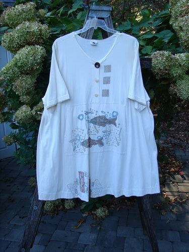 Barclay Tunnel Pocket Pull Over Dress Fish Natural Size 2 showcases a loose, cream tunic with fish motif, square prints, and a decorative button, featuring a kangaroo pocket and drawcord.
