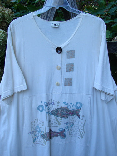 Barclay Tunnel Pocket Pull Over Dress Fish Natural Size 2 features a V-neck with three buttons, square appliqués, and a stylized fish motif. Made from organic cotton, it’s soft and lightweight.