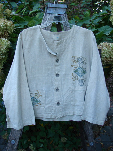 1999 Summercloth Hemp Crop Jacket Nature Cement Size 1, featuring a loose weave, collarless design, long sleeves, patch pockets with graphic prints, and metal buttons, draped on a wooden ladder outdoors.