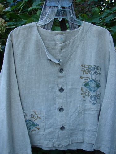 1999 Summercloth Hemp Crop Jacket Nature Cement Size 1 features a boxy, vented crop length with metal buttons, nature-inspired designs, and double front pockets, hanging outdoors against leafy plants.