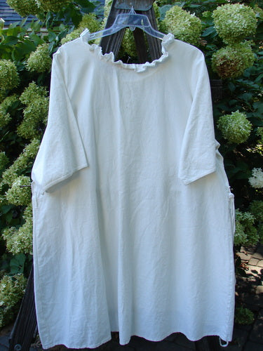 Image: A white shirt on a hanger, with a plastic hanger on a wooden surface. 

Alt text: Barclay Linen Duet Sunrise Dress, unpainted creme, size 2, on a hanger.