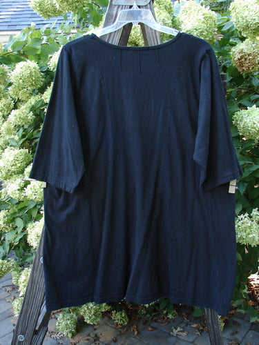 A black Barclay Sunrise Pin Tuck Pocket Tunic on a wooden pole. Features include a rounded neckline, A-line shape, short sleeves, and front pockets. Size 2, unpainted.