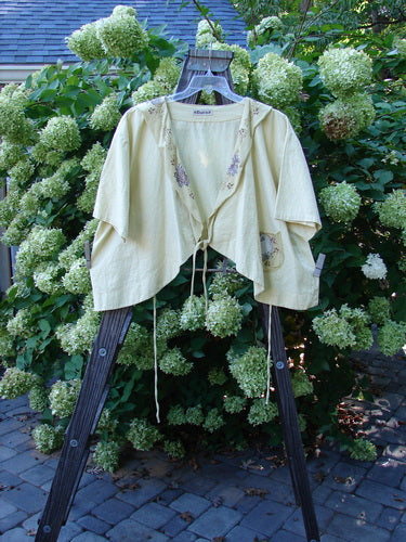 Barclay Linen Batiste Rippie Tie Jacket Shrug Florals Quiet Sunshine Size 2: A clothes rack with a white shirt featuring a floral design, alongside a close-up of a plant.