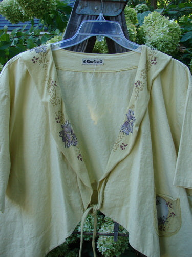 A yellow shirt with a floral design and a tie on it, from the Barclay Linen Batiste Rippie Tie Jacket Shrug Florals Quiet Sunshine Size 2 collection.
