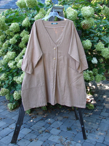 Barclay Linen Adras Uptown Jacket Unpainted Pastel Rosewood Size 2: A beige shirt with buttons on a swinger, featuring a deep V-shaped neckline, sectional triangular panels, pleated and banded lower sleeves and hemline, and double exterior drop front pockets. Bust 56, Waist 56, Hips 64, Sweep 80, Length 42.