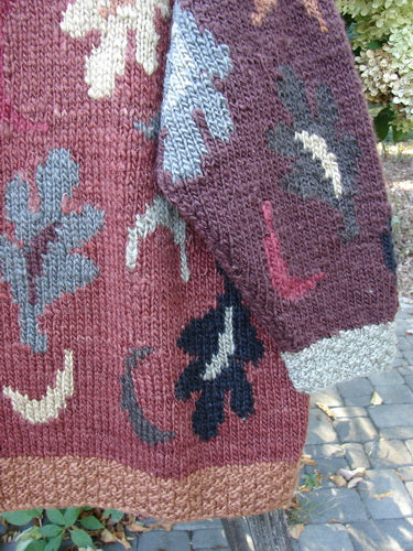 Tara Handknits Star Button Pocket Cardigan, Leaf & Moon Brights OSFA, draped on a bench, showcases intricate leaf and floral motifs. Features ribbed accents, metal star buttons, and drop pockets.