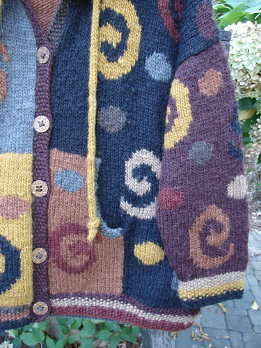 Tara Handknits Hooded Star Button Pocket Cardigan Swirls Brights OSFA features colorful blocks with swirl and dot motifs, wooden buttons, a mustard drawstring, and a cozy ribbed neckline, showcasing handcrafted detail.