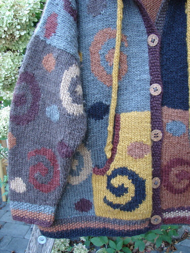 Tara Handknits Hooded Star Button Pocket Cardigan Swirls Brights OSFA features patchwork-style blocks with spiral motifs, a ribbed neckline, wooden buttons, a small front pocket, and a cozy drawcord hoodie.