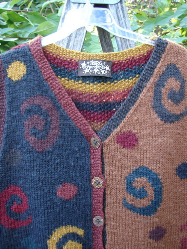 Tara Handknits Back Tab Vest Swirl Polka & Stripe Brights OSFA displayed on a wooden ladder, showcases dark slate blue and light brown color blocks with vibrant spiral-dot motifs and star metal buttons.
