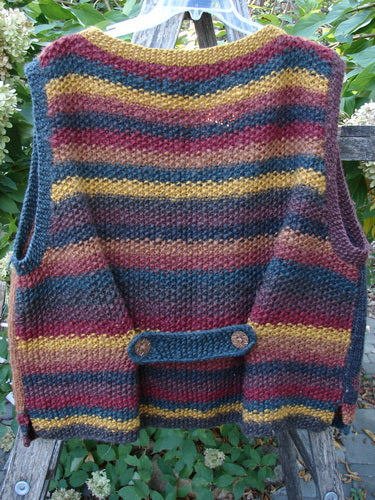 Tara Handknits Back Tab Vest Swirl Polka & Stripe Brights OSFA: A hand-knit, sleeveless vest in garter stitch with horizontal stripes, adjustable back-strap, and ribbed neckline, displayed outdoors against a wooden fence.