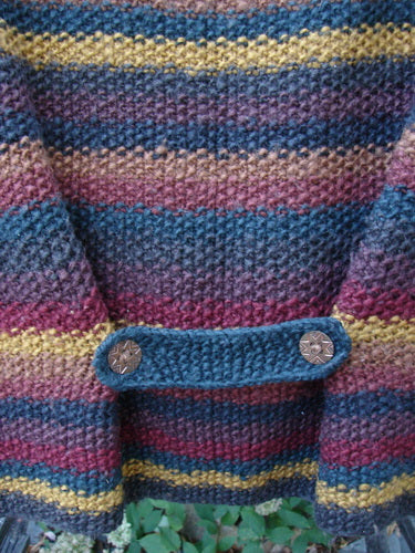 Close-up of the Tara Handknits Back Tab Vest Swirl Polka & Stripe Brights OSFA, showcasing a textured stitch with variegated yarn stripes, featuring a knitted tab and wooden-look buttons for vintage charm.