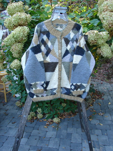 Tara Handknits Diamond Button Oversized Cardigan Geometric Naturals OSFA draped on a hanger, showcasing its patchwork argyle style with intricate patterns, contrasting knit accents, and numerous diamond-shaped metal buttons.