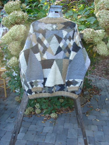 Tara Handknits Diamond Button Oversized Cardigan Geometric Naturals OSFA displayed on a wooden ladder outdoors, showcasing its intricate geometric patchwork design in muted tones, with ribbed neckline, cuffs, and metal buttons.
