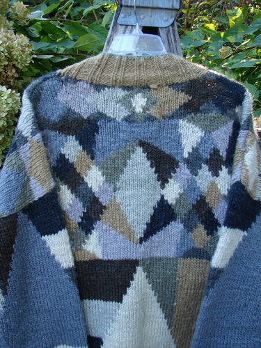 Tara Handknits Diamond Button Oversized Cardigan Geometric Naturals OSFA, showcasing an intricate argyle pattern, hangs elegantly on a clear hanger outdoors, highlighting its luxurious hand-knit craftsmanship and vintage-inspired design.