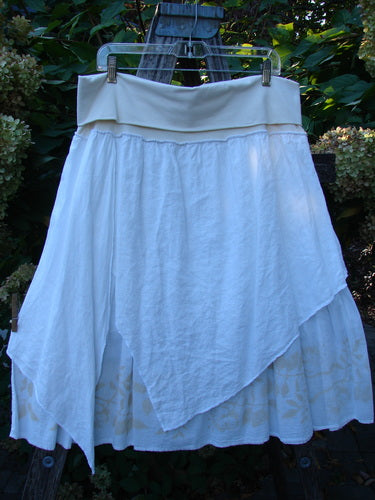 Barclay NWT Linen Fold Over Generosity Skirt Leaf Field Fresh White Size 2, featuring a wide waistband, asymmetrical batiste panels, and vine-themed paint, displayed on a wooden frame with foliage.