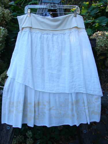 Barclay NWT Linen Fold Over Generosity Skirt Leaf Field Fresh White Size 2, features tiered layers with vine and leaf painted batiste, displayed on a hanger against leafy shrubs, highlighting its unique design.
