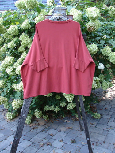A red Barclay Cotton Lycra Banded Sleeve Dolman Top on a wooden stand, showcasing its generous wide boxy shape, rounded neckline, and dolman banded lower sleeves. The vibrant color adds a significant touch to this heavy-weight organic cotton stretch fabric piece.