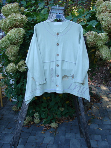 1998 Botanicals Orchard Jacket Plante Grasshopper Altered Size 1 is displayed on a wooden ladder, showcasing its mint-green hue, ¾-length sleeves, large brown buttons, and decorative hem graphics in a garden setting.