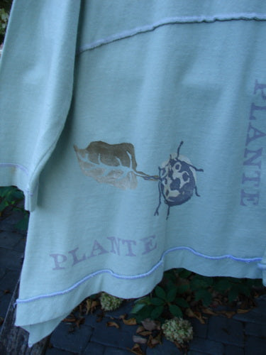1998 Botanicals Orchard Jacket Plante Grasshopper Altered Size 1: A greenish garment featuring a beetle graphic and PLANTE print, with wide banded A-line hem and pearl buttons, hanging outdoors.