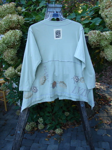 1998 Botanicals Orchard Jacket Plante Grasshopper Altered Size 1 displayed on a wooden ladder in a garden, showing its back with a stylized insect band and a signature Blue Fish patch.