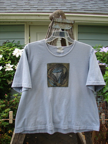 1999 Patched Short Sleeved Crop Tee Feather Bluestone Size 2 displayed on a hanger, showcasing a feminine rolled neckline, classic feather paint design, and Blue Fish patch, made from mid-weight organic cotton.