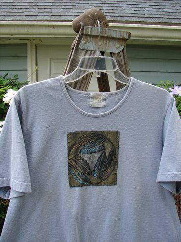 1999 Patched Short Sleeved Crop Tee Feather Bluestone Size 2 displayed on a hanger, featuring a signature Blue Fish patch and classic 1999 feather theme paint, with a thinner feminine rolled neckline.