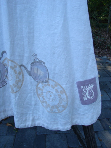 1999 NWT Cream and Sugar Coat Tea Time Teadye OSFA features a graphic print of vintage teapots pouring into plates along the hem, with a purple patch logo, draped outdoors on a bench.