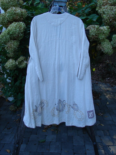 1999 NWT Cream and Sugar Coat Tea Time Teadye OSFA: A long, cream-colored linen jacket with whimsical tea-themed prints, featuring deep side pockets and a single oversized shell button, hanging outdoors.