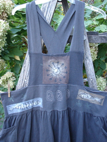 1995 Overall Jumper Fish Space Briquette OSFA hanging outdoors on a wooden ladder, showcasing its crisscross back straps, gathered skirt, hand-painted abstract motifs, oversized side pockets, and Blue Fish Patch.