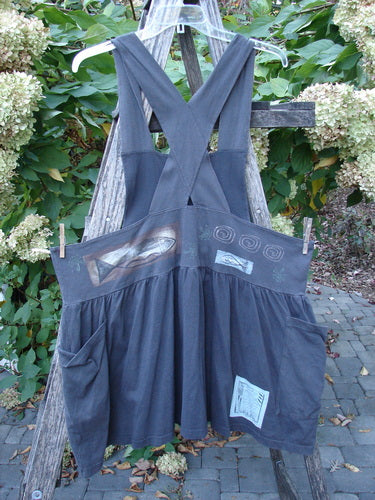 1995 Overall Jumper Fish Space Briquette OSFA, featuring crisscross straps, a gathered skirt, and oversized pockets, with a whimsical fish and space theme, displayed on a wooden trellis outdoors.