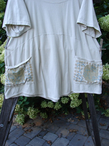 A white shirt with pockets on a clothes rack, part of the Barclay Be There Top Moon Twig Dust Size 2 collection. Made from organic cotton, this top features a deeper neckline, empire waist seam, full pleats, and a skirt flair. Painted in the Moon and Twig theme, it offers a sweet drape and spin. Bust 54, waist 56, hips 60, hem circumference 80, and length 32 inches.