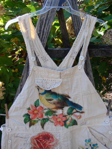 Magnolia Pearl Applique Benjamin Overall Birdie Bouquet Moon OSFA hangs outdoors, featuring colorful bird and floral imagery on light-cream fabric, adjustable straps, and distressed details, embodying BlueFishFinder's vintage, expressive style.