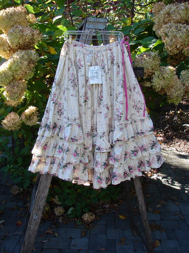 Magnolia Pearl Penelope Skirt Des Rosiers Floral Idealist OSFA, featuring a tiered, ruffled hem and floral print, hangs on a step-ladder, showcasing the skirt's drawstring waist and intricate lace detailing.