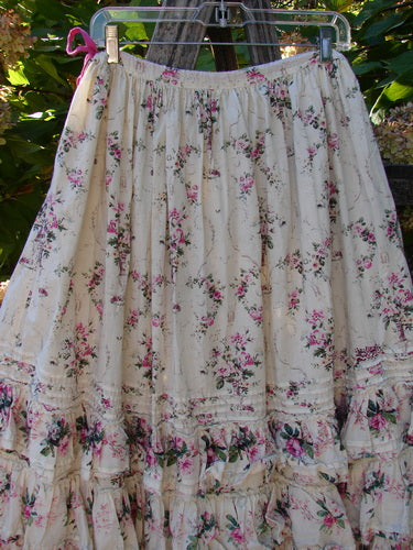 Magnolia Pearl Penelope Skirt Des Rosiers Floral Idealist OSFA features cream cotton with pink-green rose sprays, lace-trimmed ruffles, and a drawstring waist, hanging outdoors, exuding vintage charm from Bluefishfinder.com.